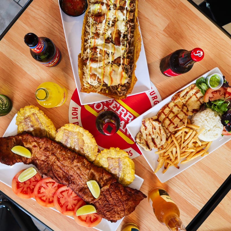 An overhead view of a table laden with La Perrada's burgers, fried fish, chicken, fries, and drinks.