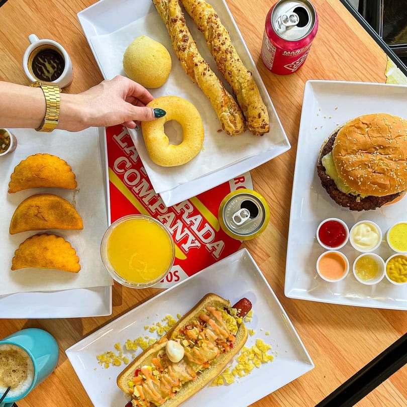 Overhead view of a table laden with La Perrada burgers, hot dogs, empanadas, and drinks.