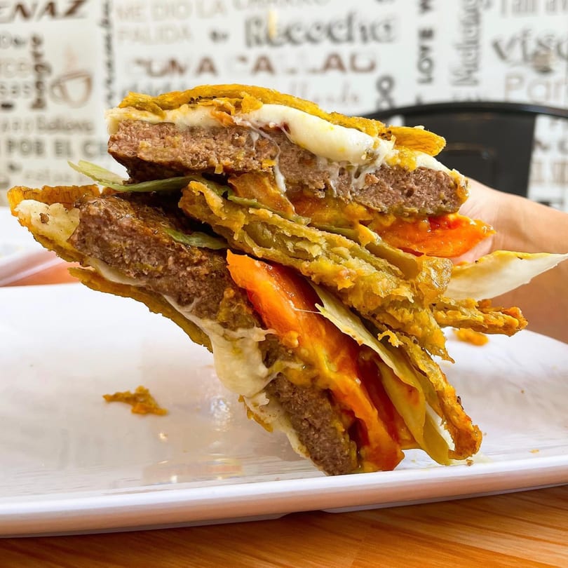 A La Perrada burger with a thick patty, melted cheese, tomatoes, and plantain buns.
