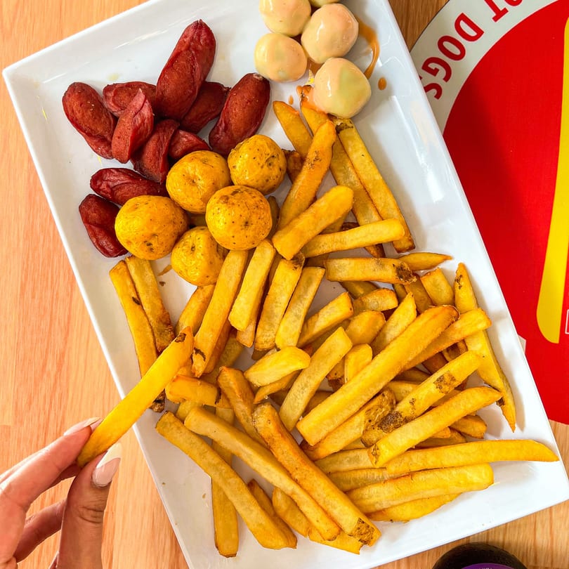 A plate of La Perrada's fries, sausages, and small yellow potatoes, with a hand picking up a fry.