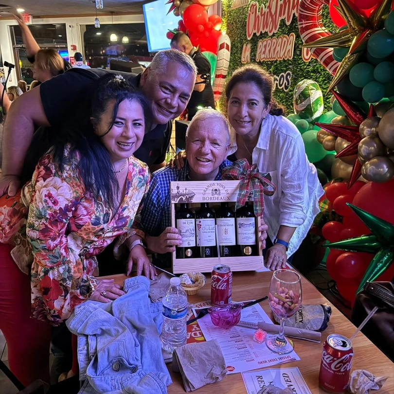 Four smiling adults pose with a wine gift box at La Perrada, surrounded by festive Christmas decorations.